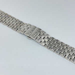 Könnte beinhalten: Ein silbernes Metallarmband mit gebürsteter Oberfläche. Das Armband besteht aus einzelnen Gliedern, die miteinander verbunden sind.