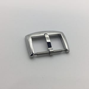 May include: A silver metal watch band buckle with a polished finish.