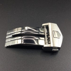May include: A silver metal watch band clasp with a polished finish and a push-button release.
