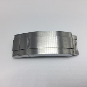 Puede incluir: Un cierre de pulsera de reloj de metal plateado con acabado cepillado.