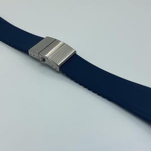May include: A navy blue watch strap with a stainless steel clasp. The strap is made of a flexible material and has a textured underside. The clasp is a brushed metal finish.