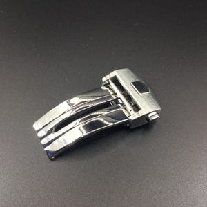 May include: A silver watch band clasp with a polished finish and a three-piece design.