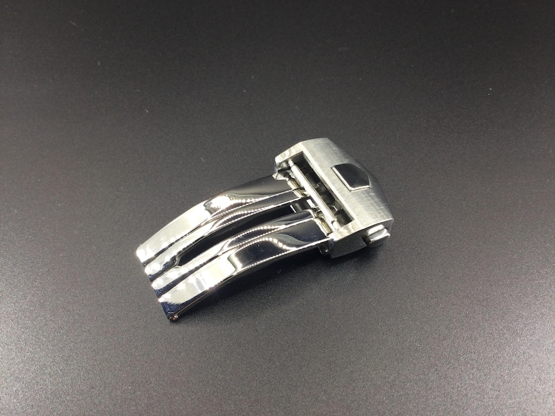 May include: A silver watch band clasp with a polished finish and a three-piece design.