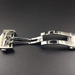 May include: A silver metal watch band clasp with a double-locking mechanism.