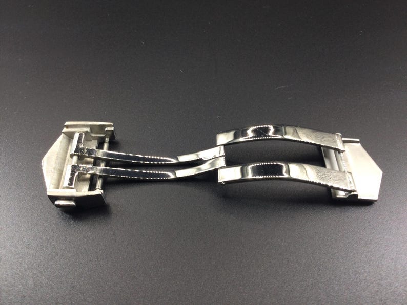 May include: A silver metal watch band clasp with a double-locking mechanism.