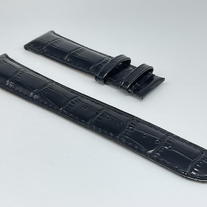 Puede incluir: Dos correas de reloj de cuero negro con un patrón de cocodrilo. Las correas están hechas de un material liso y brillante.