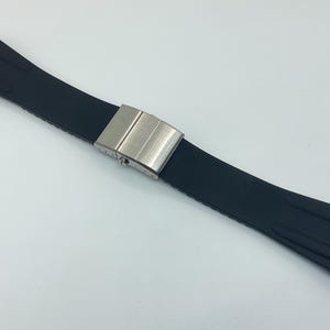 May include: A black rubber watch strap with a silver buckle. The strap has a textured design and is designed for a watch with a lug width of 20mm.