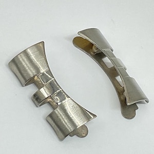 May include: Two silver metal watch band end pieces. The end pieces are curved and have a brushed finish.
