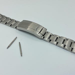 May include: A silver watch band with a brushed finish and a clasp. The band is made of metal and has a polished finish. Two silver spring bars are included.