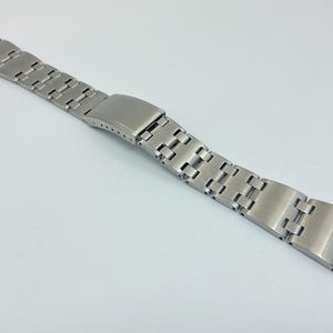 May include: A silver metal watch band with a brushed finish. The band is made of individual links that are connected together.