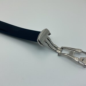 May include: A black rubber watch strap with a silver buckle and deployment clasp.