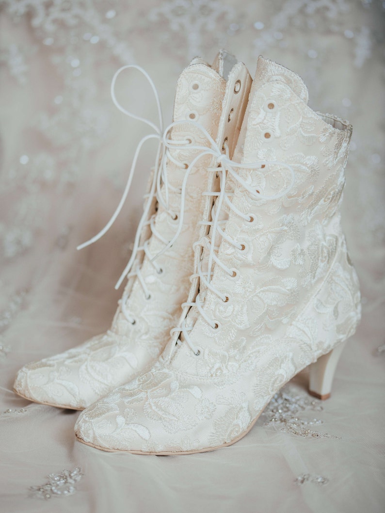 Pode incluir: Um par de botas de tornozelo brancas de renda com um delicado padr&atilde;o floral. As botas t&ecirc;m um salto alto e fechos de renda.