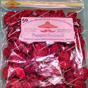 May include: A transparent bag containing dried, red Carolina Reaper chillies. The label reads "50 Premium Whole Dried Carolina Reapers" and "PepperliciousS". The label also includes the text "Please use caution when handling and eating. ENJOY!"