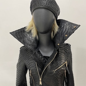 以下が含まれることがあります： 大きな襟、ジッパー留め、金色のアクセントが付いた黒い革のジャケット。ジャケットはヘビ革製で、金色の王冠のバックルが付いたベルトが付いています。