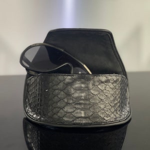 May include: A black leather sunglasses case with a snakeskin pattern. The case is open and a pair of black sunglasses are inside.