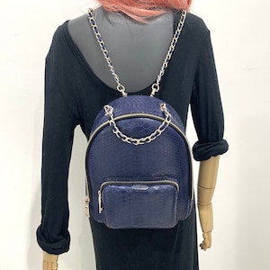 May include: A dark blue faux leather backpack with a chain strap. The backpack has a small pocket on the front.