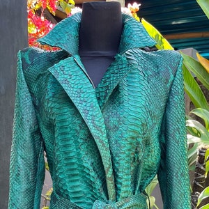 May include: A long, green snakeskin trench coat with a belt. The coat is on a mannequin and has a dark green snakeskin pattern.