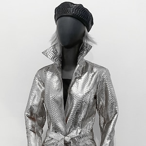 以下が含まれることがあります： ベルト付きの長い銀色のヘビ革のコート。コートはVネックで長袖です。