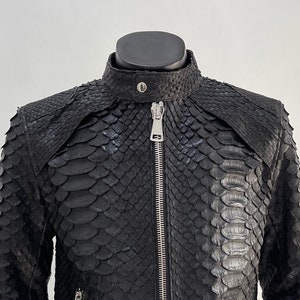 以下が含まれることがあります： ヘビ柄の黒い革のジャケット。ジャケットはジッパーで閉まり、前面にポケットが2つ付いています。