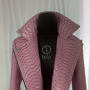 May include: A pink snakeskin leather jacket with a zipper closure and a collar. The jacket is on a mannequin and has a label that says "beltp".
