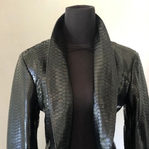 Peut inclure: Une veste en cuir de serpent noir avec un col large et des manches longues.