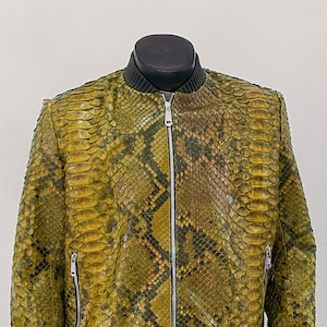 以下が含まれることがあります： ジッパー留めの緑と茶色のヘビ革ボンバージャケット。ジャケットはリブ編みの襟と袖口があります。