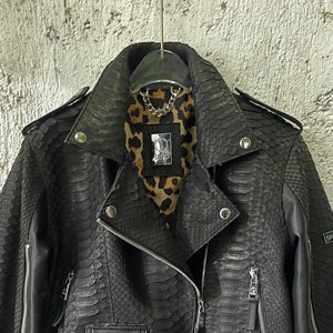 May include: Black leather jacket with a snakeskin pattern. The jacket has a zipper closure, two pockets, and a silver zipper pull. The lining of the jacket is leopard print.