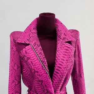 May include: A pink snakeskin jacket with a zipper closure and a belt. The jacket has a collar and long sleeves.