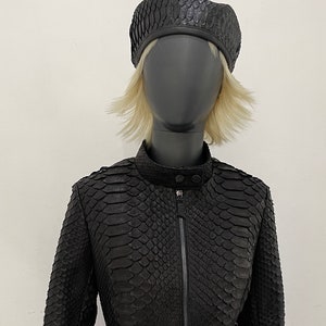 以下が含まれることがあります： マネキンに展示された黒革のジャケットとベレー帽のセット。 ジャケットはジッパー開閉で、ヘビ革のような質感の模様が特徴です。 ベレー帽はジャケットのデザインとマッチしています。 マネキンはピンクのスカートを着用しています。