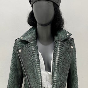 以下が含まれることがあります： ジッパー留めとウエストにベルトが付いた緑色のヘビ革のバイクジャケットです。