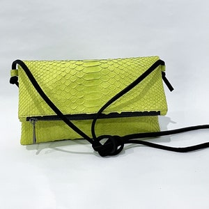 May include: A bright green snakeskin crossbody bag with a black strap. The bag has a flap closure and a zipper detail.