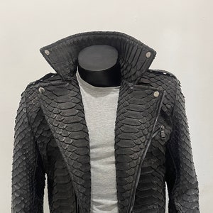 May include: A black leather jacket with a zipper closure and a belt. The jacket is made of snakeskin and has a stand-up collar.