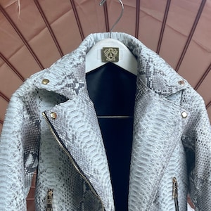 May include: A white and gray snakeskin leather motorcycle jacket with a zipper closure and a belt at the waist.