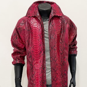 Peut inclure: Un long manteau en peau de serpent rouge avec une fermeture éclair. Le manteau a un col montant et des manches longues.