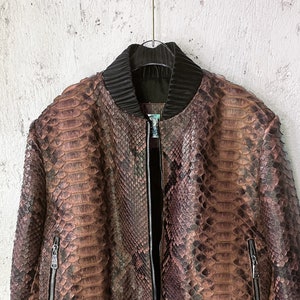 May include: A brown snakeskin bomber jacket with a black ribbed collar, cuffs, and waistband. The jacket has a zip closure and two zipped pockets.