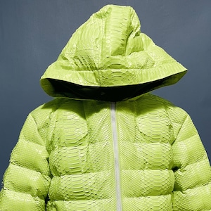 以下が含まれることがあります： ジッパーとフードが付いた、ライムグリーンのヘビ革製パファージャケットです。