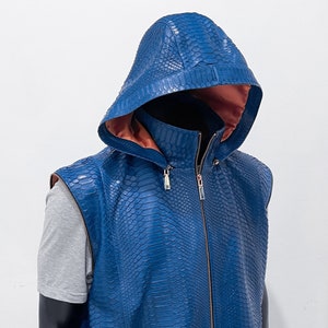 以下が含まれることがあります： ジッパー留めとフード付きの襟が付いた青いヘビ革のベスト