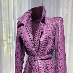 May include: A purple snakeskin jacket with a belted waist and a zip closure. The jacket has a collar and long sleeves.