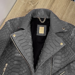 May include: A grey snakeskin leather biker jacket with a zip fastening and gold hardware. The jacket has a '1919' logo on the left side of the chest.