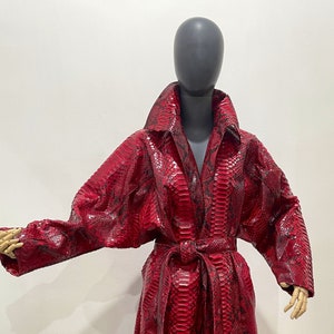 Peut inclure: Un long manteau en peau de serpent rouge avec un motif noir. Le manteau a une ceinture et un col.