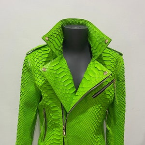 以下が含まれることがあります： 明るい緑色のヘビ革のジャケットで、ジッパー留めと金色の金具が付いています。