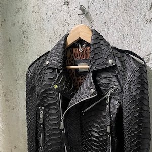 May include: Black leather jacket with a snakeskin pattern. The jacket has a zipper closure and multiple pockets.