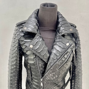 以下が含まれることがあります： ヘビ柄の黒い革のジャケット。ジッパー留め、ベルト、スタンドカラーです。