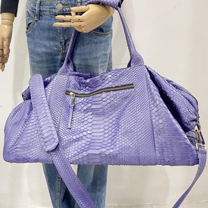 May include: A purple snakeskin leather duffel bag with a long shoulder strap. The bag has a zipper closure and a small pocket on the front.