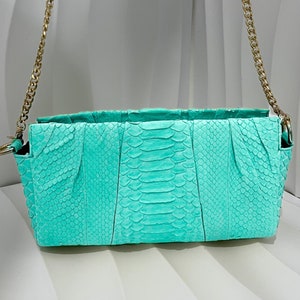 May include: A turquoise snakeskin clutch bag with a gold chain strap.