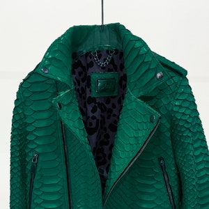 以下が含まれることがあります： ジッパー留めの緑色のヘビ革のバイクジャケット。ジャケットは丈が短く、長袖です。