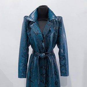 May include: A teal and black snakeskin-patterned trench coat with a matching belt. The coat has a notched collar, long sleeves, and a zip-up front. The coat is displayed on a black mannequin.