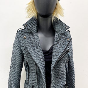 以下が含まれることがあります： ジッパー留めとベルトが付いた青いヘビ革のジャケット。ジャケットはスタンドカラーと長袖です。