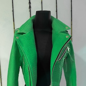 以下が含まれることがあります： スタンドカラーのジッパー留め、鮮やかな緑色の革のジャケット。ジャケットはヘビ革製です。