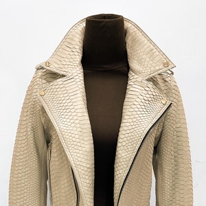 May include: A beige leather jacket with a snakeskin pattern and gold zipper accents.